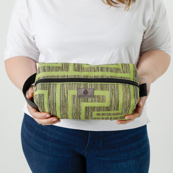 A woman holding a lime green geometric pattern toiletry kit with a gray Unshattered label named after Kristie