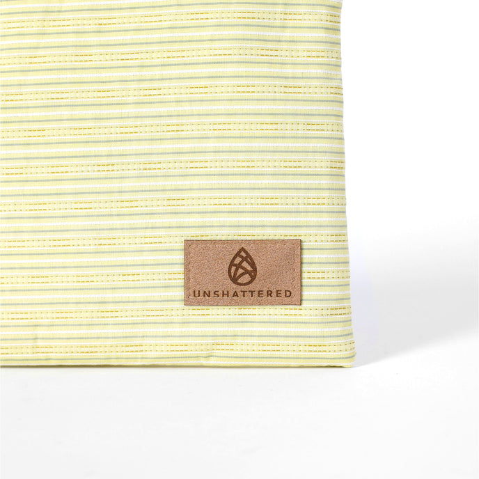 Tan suede Unshattered label on a light yellow striped zippered pouch on a white background