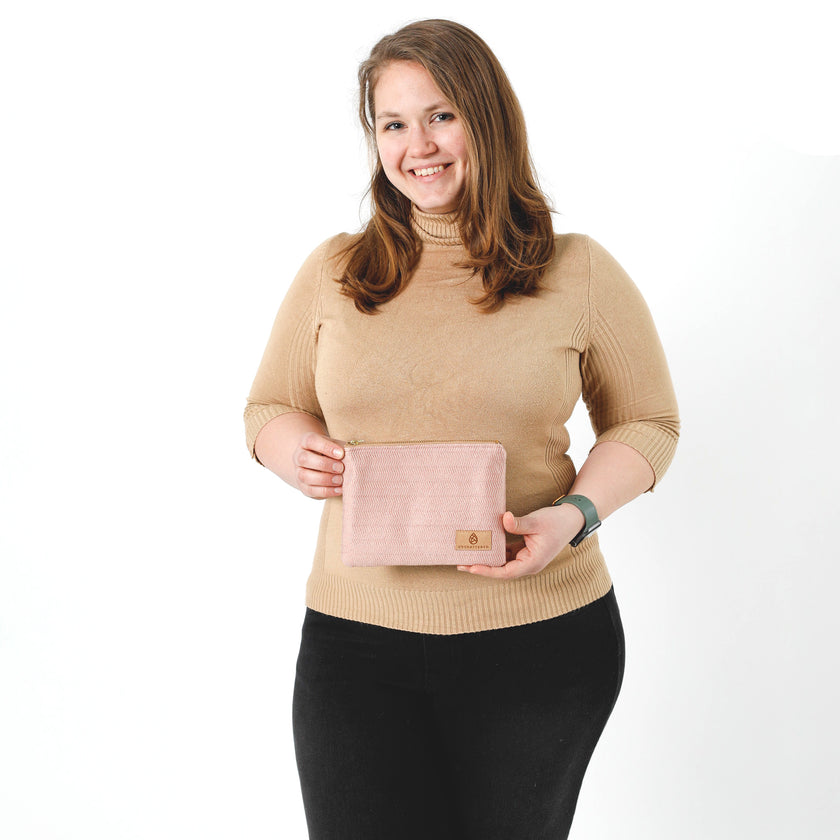 A woman holding a pink line design zip pouch wearing a tan turtle neck top and black skirt named after Lakota