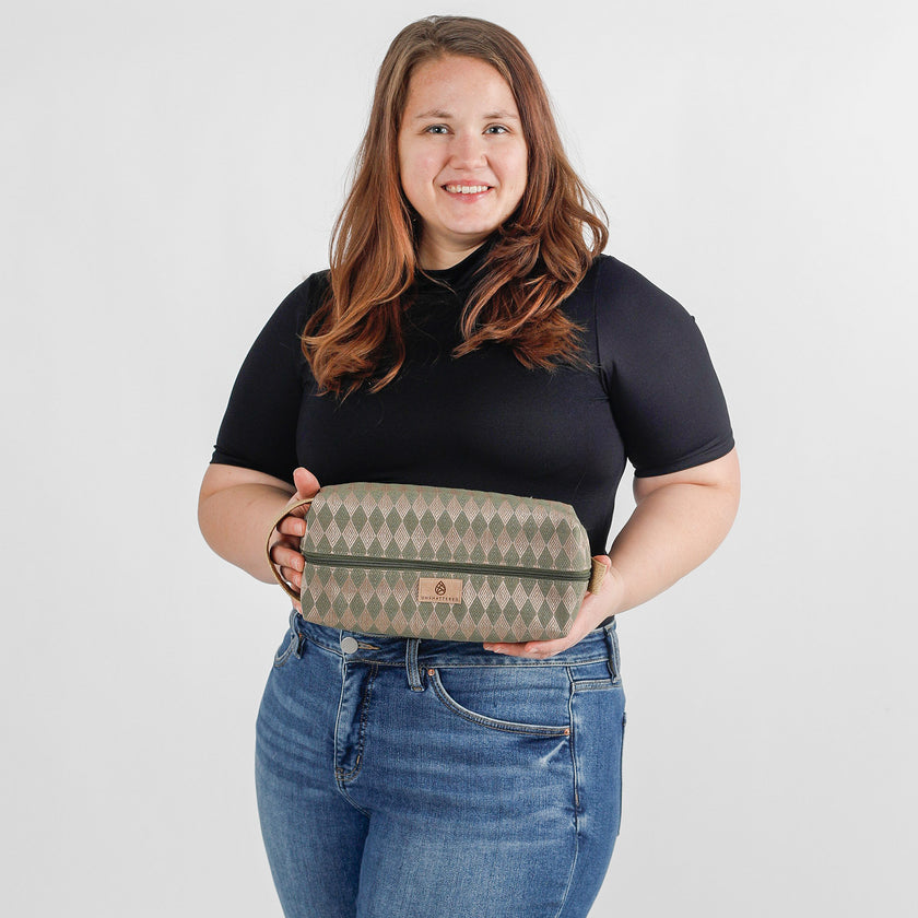 A woman holding a  green geometric patterned toiletry kit with a tan Unshattered label 