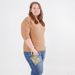 Woman wearing a beige sweater and blue jeans holding a floral patterned clip pouch against a white background