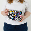 A woman holding a fun vibrant design zip pouch with a gray label and silver hardware named after Lella