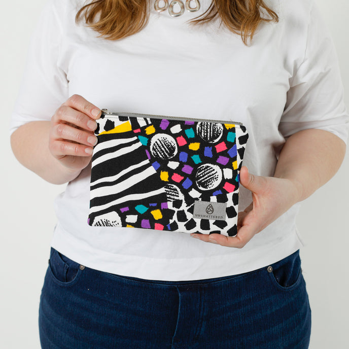 A woman holding a fun vibrant design zip pouch with a gray label and silver hardware named after Lella