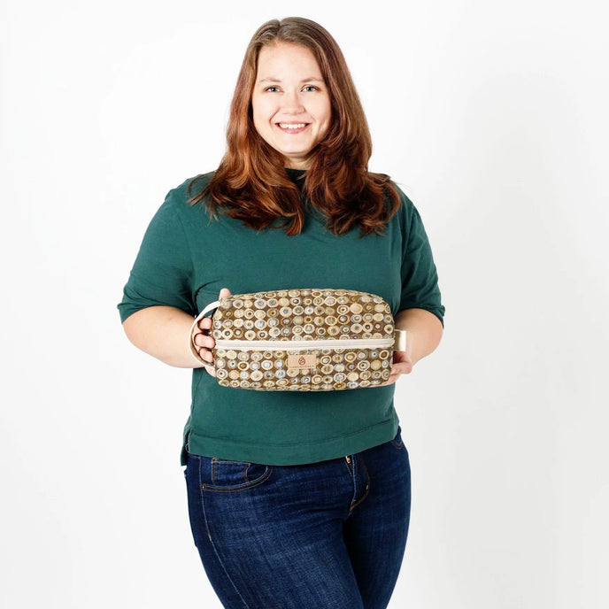 Woman holding a patterned toiletry kit against a plain background