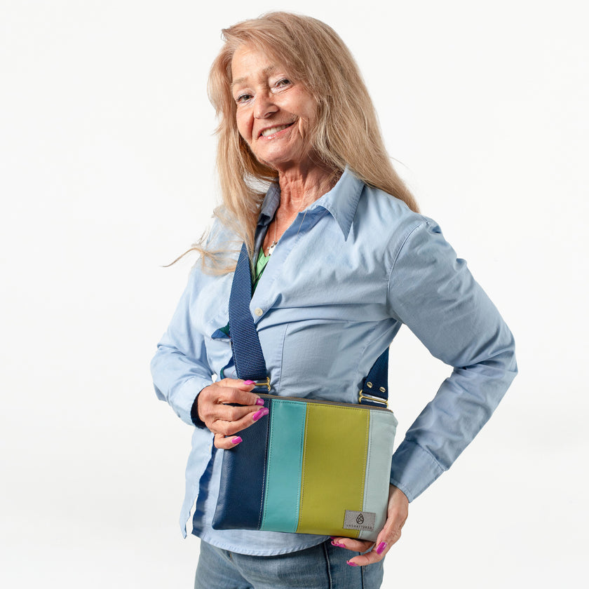 A woman wearing this brand signature multi-panel crossbody bag with blue, teal, green and powder blue luxury leather alternative material with a dark blue strap 