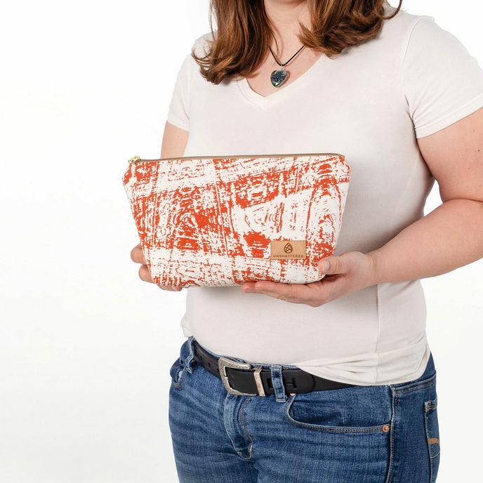 A woman holding a burnt orange swizzle makeup kit with a tan Unshattered label
