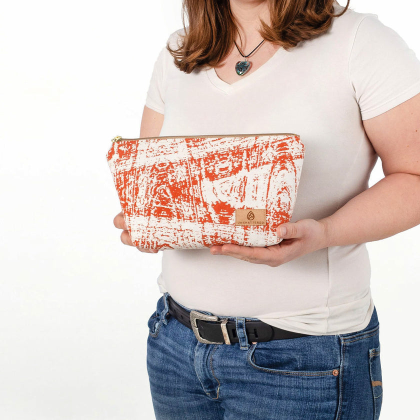 A woman holding a burnt orange swizzle makeup kit with a tan Unshattered label