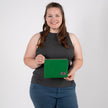 A woman smiling while holding a textured green fabric zip pouch featuring a gray label and a matching gray zipper.