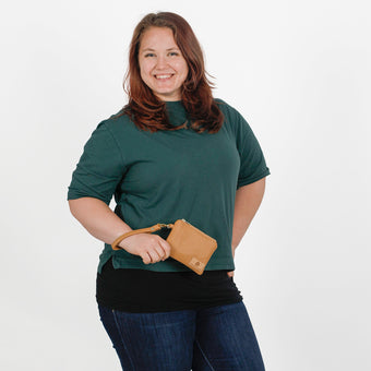 Woman holding brown luxury leather alternative clip pouch while wearing a green shirt on a white background