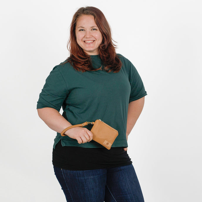 Woman holding brown luxury leather alternative clip pouch while wearing a green shirt on a white background
