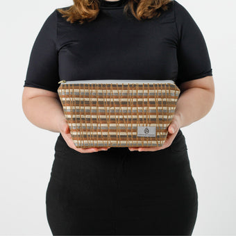 A woman holding a makeup bag with gray, golden yellows, and earthy browns interwoven with shimmering gold accents with a gray label named after Jennifer