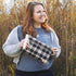 Woman holding a plaid bag in front of tall grass named after Jenny