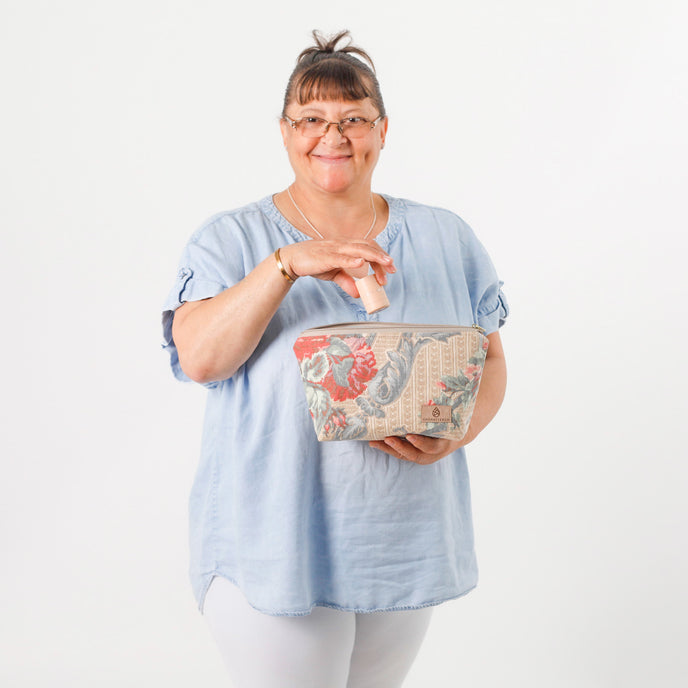 A woman holding a flower makeup kit with a jean top and white jeans on smiling named after Antionette
