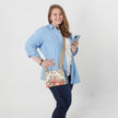 A woman holding a cell phone showing hands free wearing a flower crossbody bag named after Helene