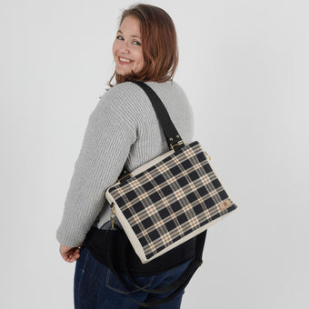 A woman carrying a black/coffee plaid convertible handbag named after Jeanne 