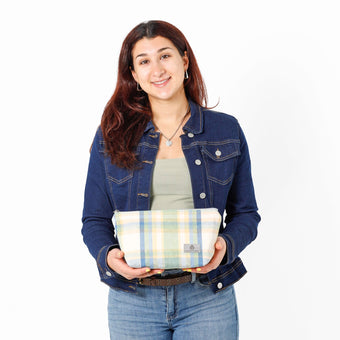 A woman holding a blue plaid makeup bag wearing a green top with jean jacket  named after Mary 