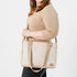 A woman wearing a tan sweater carrying a Hayley convertible handbag with a beige leather-like material and pink and white upcycled fabric, featuring gold-tone hardware and an adjustable crossbody strap.