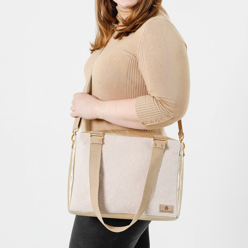 A woman wearing a tan sweater carrying a Hayley convertible handbag with a beige leather-like material and pink and white upcycled fabric, featuring gold-tone hardware and an adjustable crossbody strap.