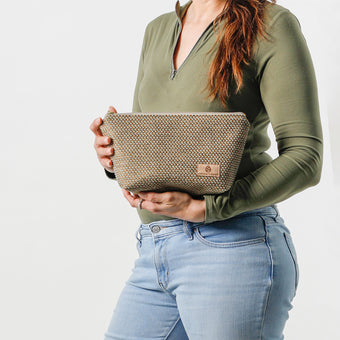 Person holding a neutral fabric makeup kit against a white background