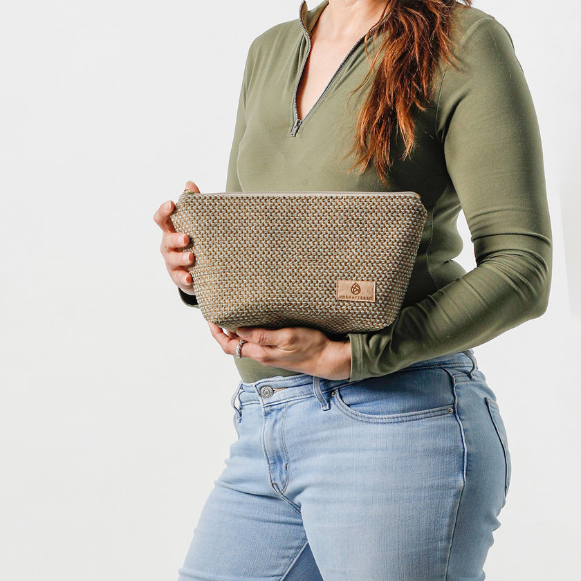 Person holding a neutral fabric makeup kit against a white background