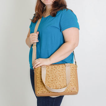 A woman carrying a yellow patterned convertible handbag with tan straps and gold hardware named after Quadira 