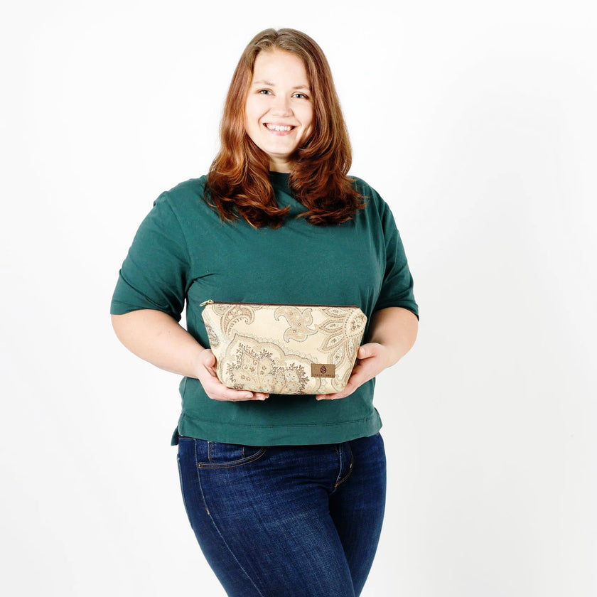 Woman holding a paisley makeup kit with seafoam green accents against a plain background