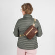Person wearing a gray puffer jacket with a brown errand crossbody bag on a white background