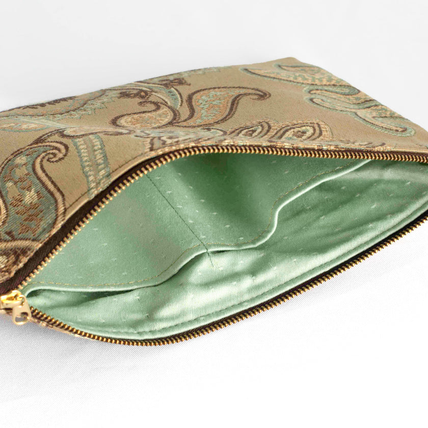A mint green interior with a gold tone zipper on a tan floral large zip pouch on the exterior