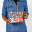 A woman holding a blue floral zip pouch with a tan Unshattered label 