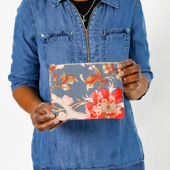 A woman holding a blue floral zip pouch with a tan Unshattered label 