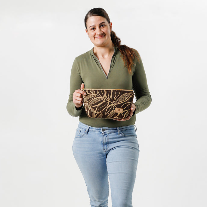 Woman holding an eye-catching brown leaf patterned fabric makeup bag on a white background. 