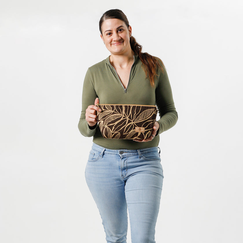 Woman holding an eye-catching brown leaf patterned fabric makeup bag on a white background. 