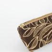 Tan zipper with gold hardware on a brown leaf patterned fabric makeup bag on a white background. 