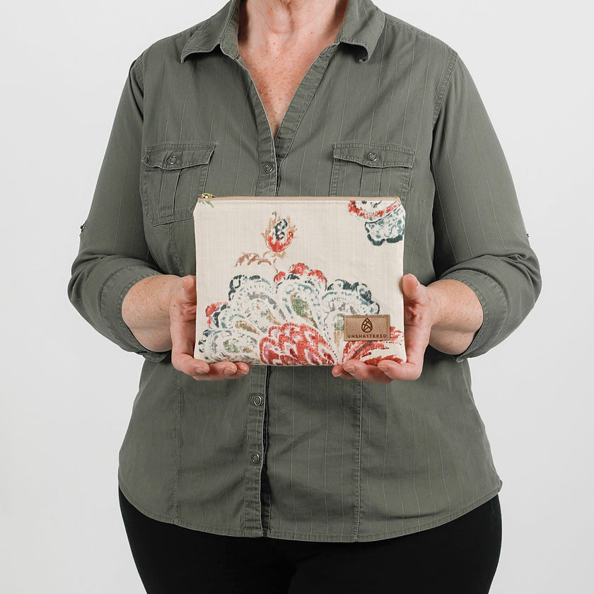 A woman holding a floral pattern zip pouch with a tan label 