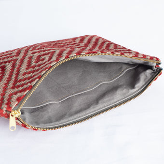 A gray interior fabric on a red maze design on exterior with a gold tone zipper 