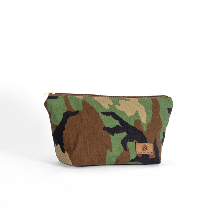 A makeup bag handcrafted from upcycled woodland camouflage uniforms with a brown label and gold tone zipper