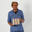 A woman holding a yellow and blue striped zip pouch wearing a jean shirt, named after Marcia 