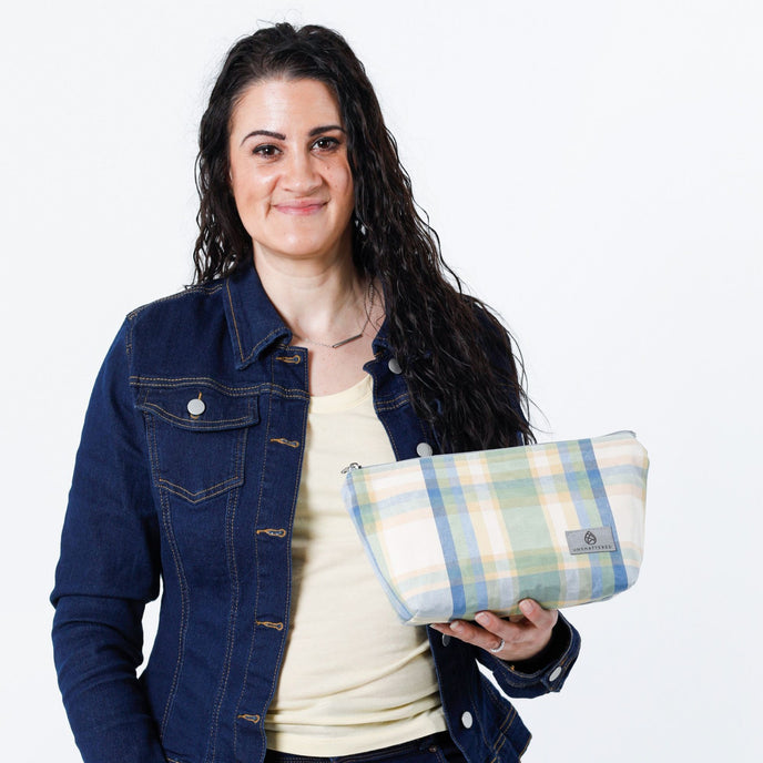 A woman holding a blue picnic plaid makeup bag with a jean jacket named after Mary 