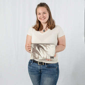 A woman holding a large zip pouch with white and grays design with a gray label 