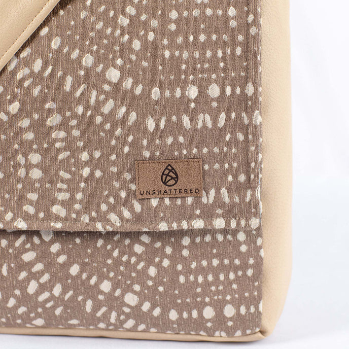A brown label on a beige and brown circle pattern large messenger bag 