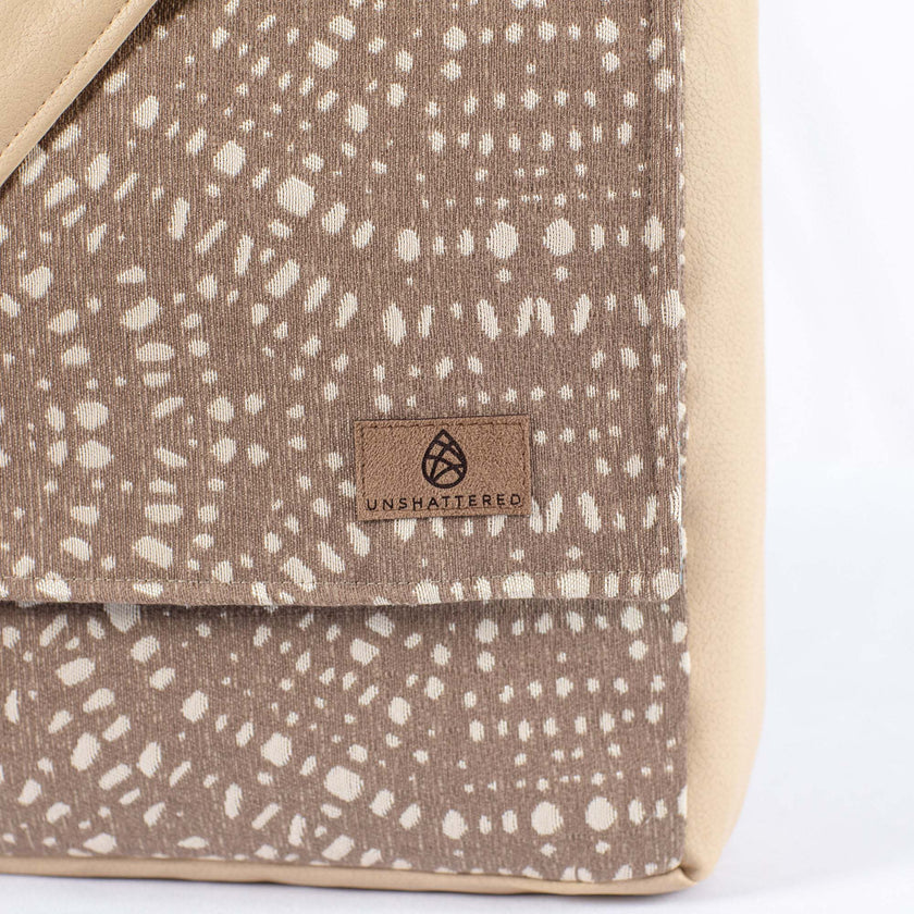 A brown label on a beige and brown circle pattern large messenger bag 