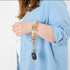 A woman carrying a  multicolored floral key clip with a gold-tone push gate clip and a tan label that reads 'UNSHATTERED' named after Bianca 