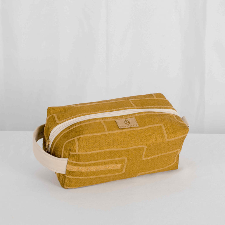 A gold-colored toiletry kit with a white zipper and leather alternative handle on a white background.