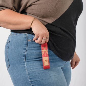 A woman holding a red loop keychain with a dragonfly in gold a tan label and gold hardware 