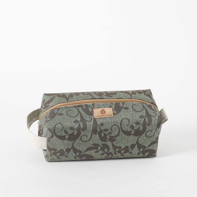 A green and brown geometric patterned toiletry kit with a white zipper and a brand tag 