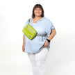 A woman wearing a lime green errand bag across her chest smiling, bag named after Nadine 