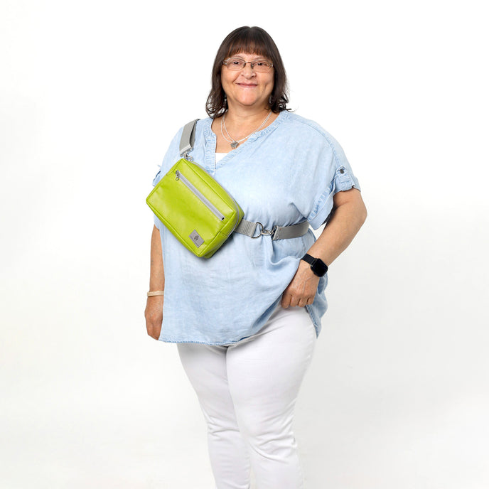 A woman wearing a lime green errand bag across her chest smiling, bag named after Nadine 