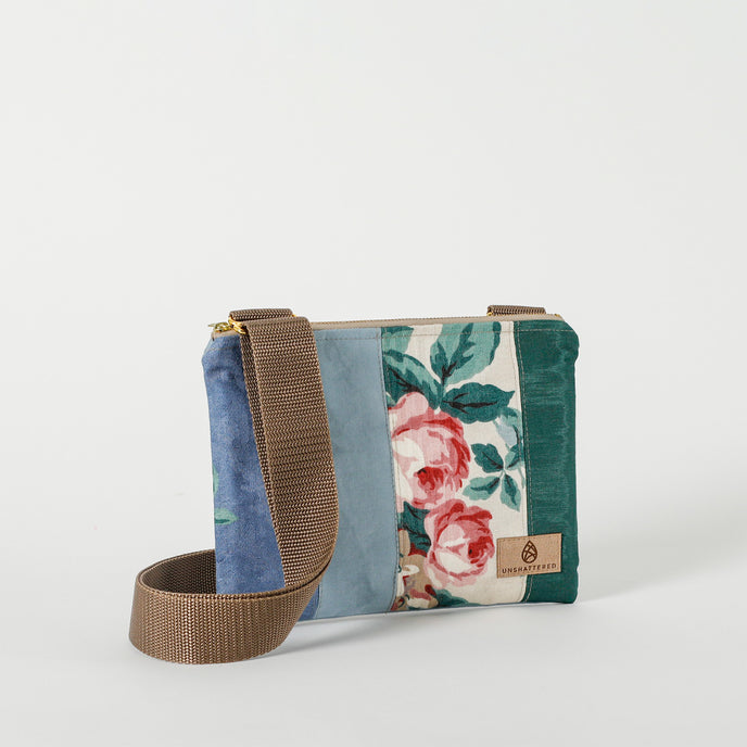 A multi-panel crossbody pouch with a floral design, featuring panels in varying shades of blues and greens, and a brown crossbody strap named after Nadiya 