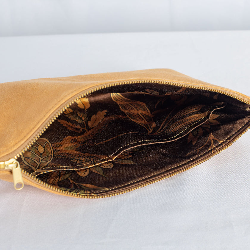 A floral brown interior fabric on a tan suede large zip pouch with a gold tone zipper