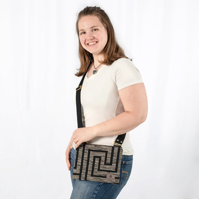 Woman holding a black and brown geometric patterned crossbody pouch against a white background named after Nikki 